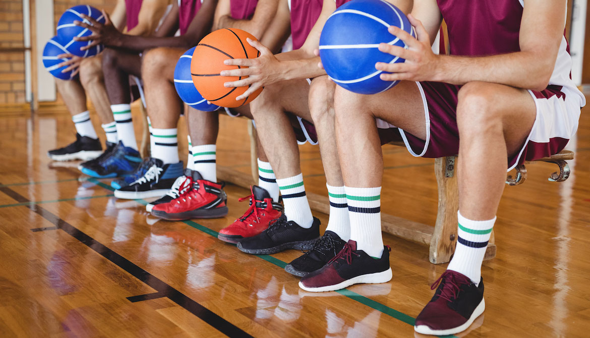 basketball players sitting on a bench holding basketballs