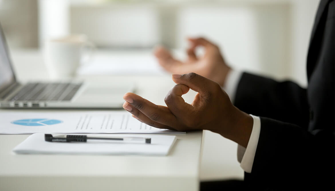 businessman meditates at his desk to practice better mental health in the workplace