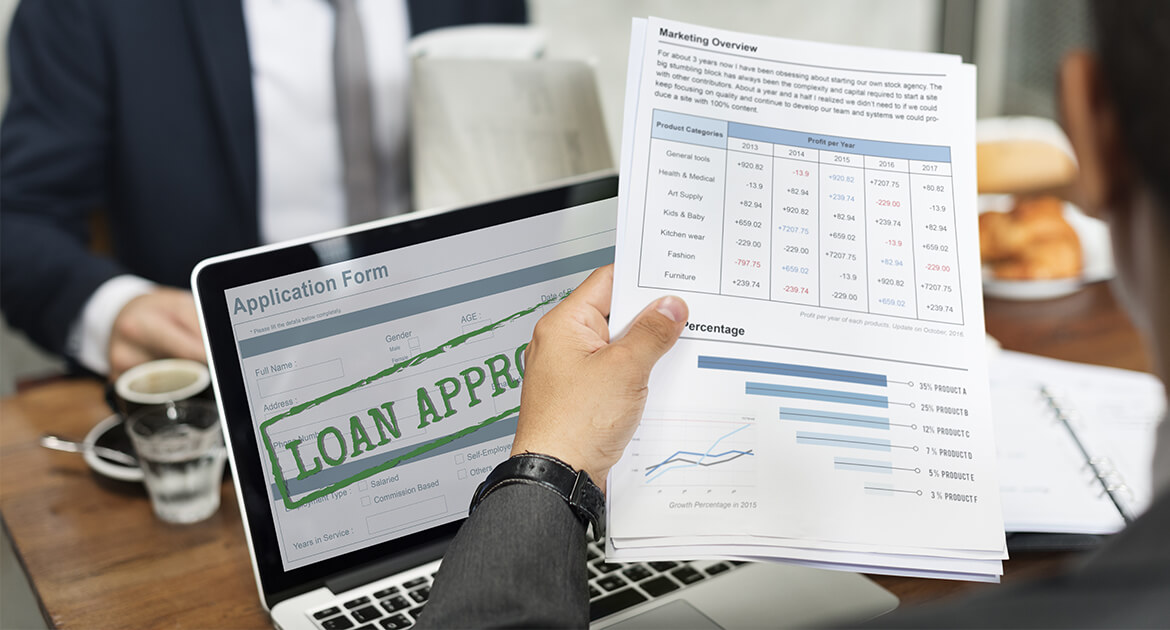 two businessmen working on a marketing plan over a laptop that displays Loan Approved