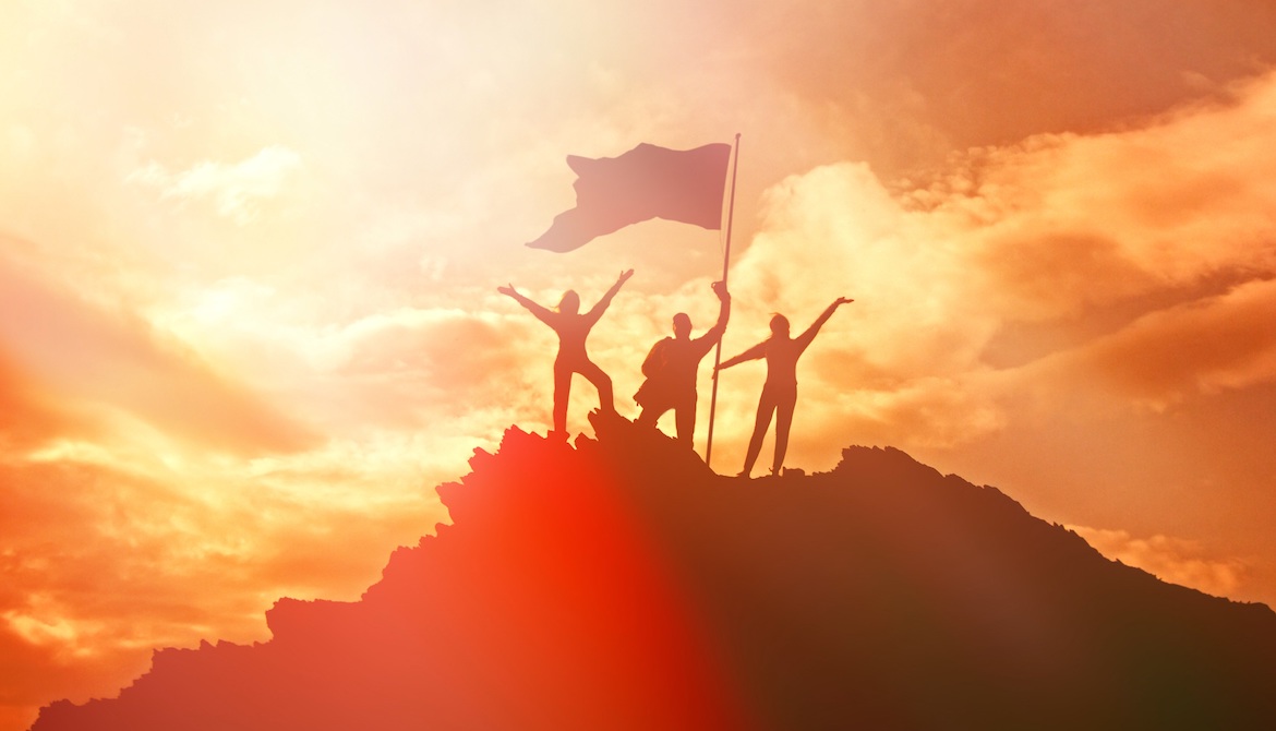 Group of people raising a flag at the top of a mountain symbolizing high performance and success