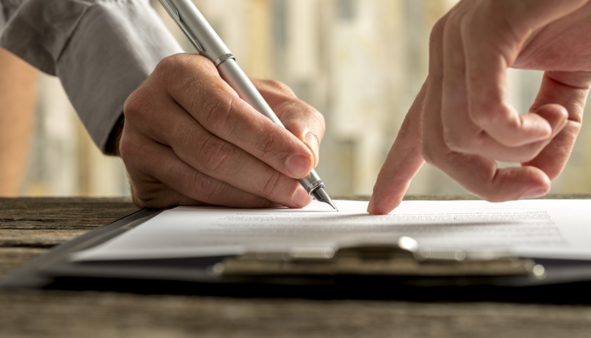 hand pointing to a contract that another businessman is about to sign