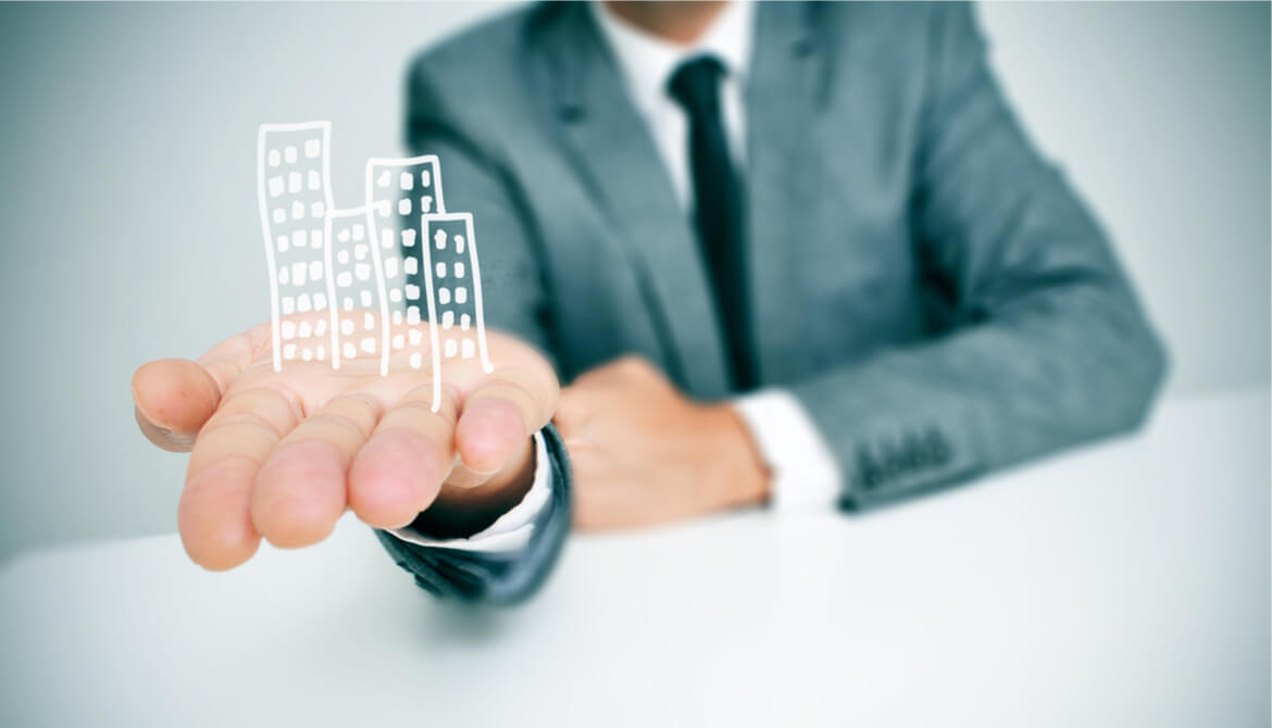 a businessman sitting in a desk showing a pile of drawn buildings in his hand