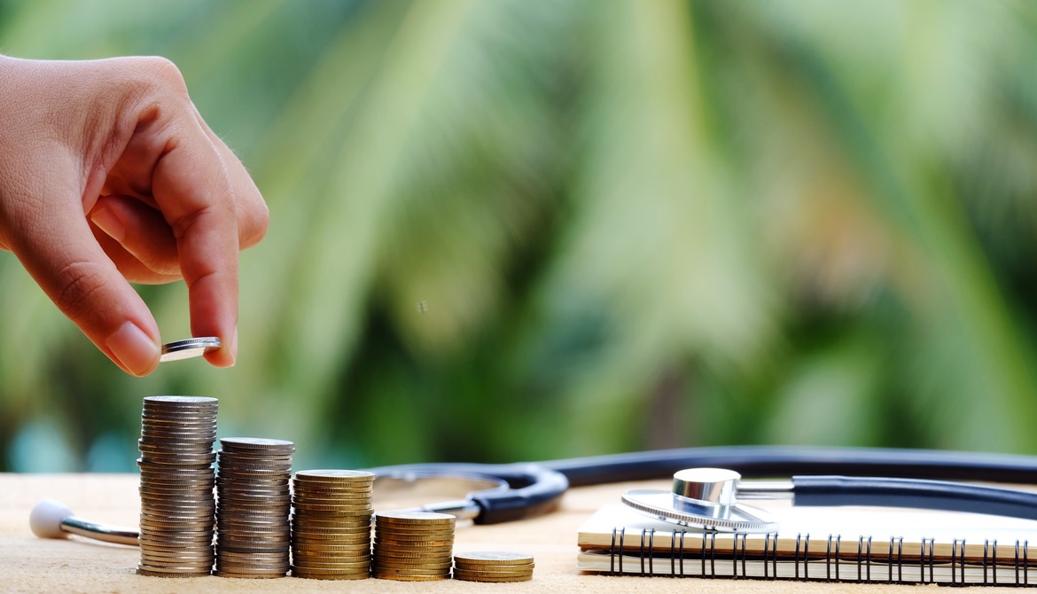 hand adding to stacks of coins next to a notebook and stethoscope representing financial wellness