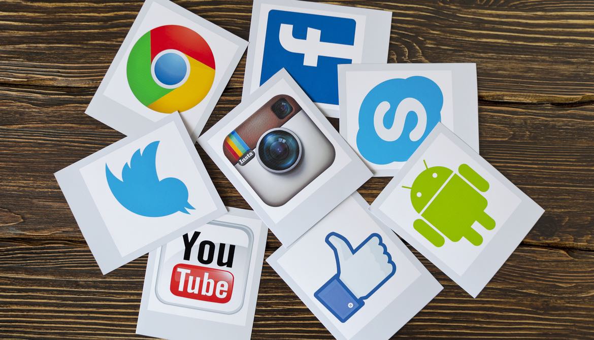 social media icons printed on sheets of paper scattered on a wood surface