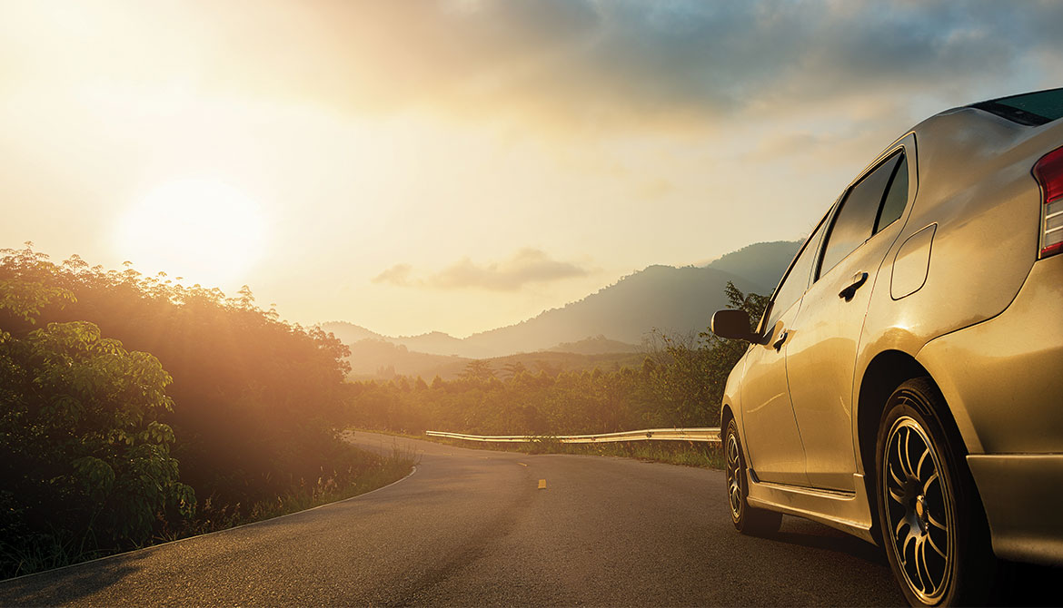 car driving along rough winding road toward distant hills at sunrise