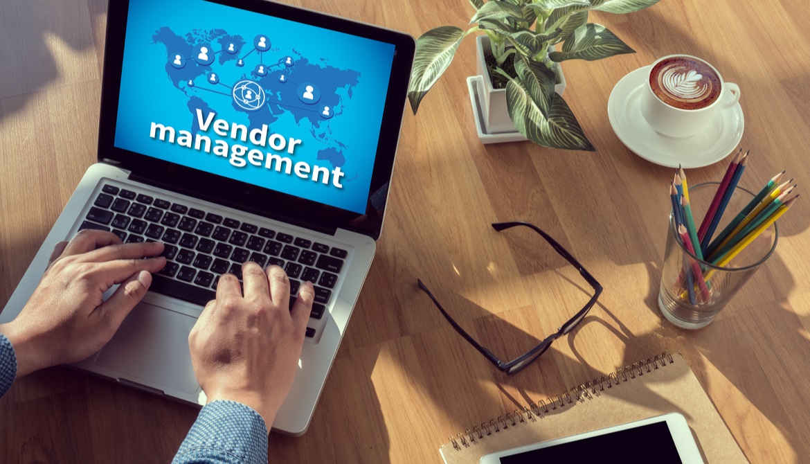 person reviewing vendor management chart on laptop sitting on wooden desk