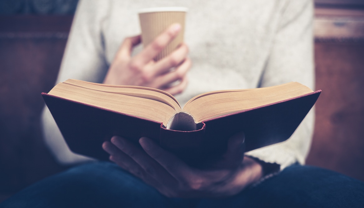 young leader reading a red hardcover book while holding a paper coffee cup