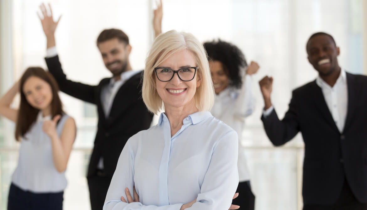 smiling female executive with team celebrating behind her