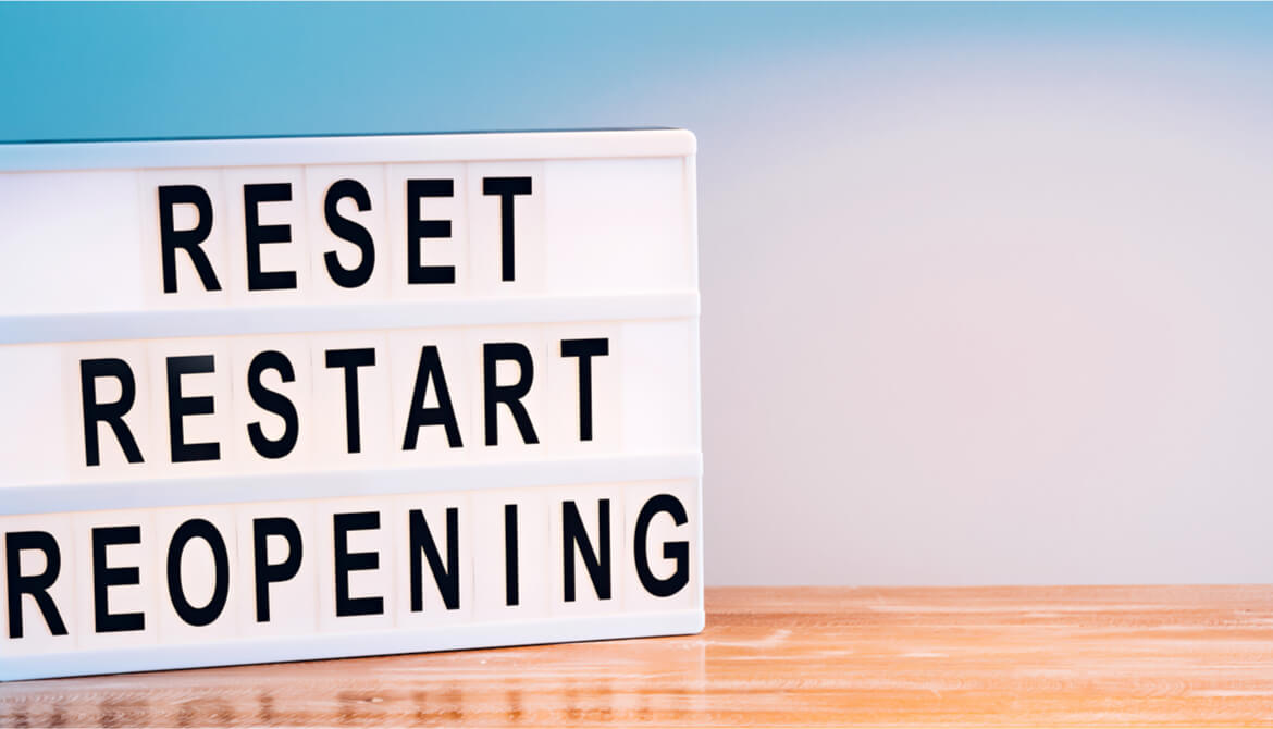 reset restart reopening sign on wooden table in front of blue background