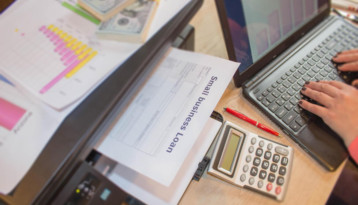 Businesswoman types on laptop displaying financial chart while printing small business loan application form