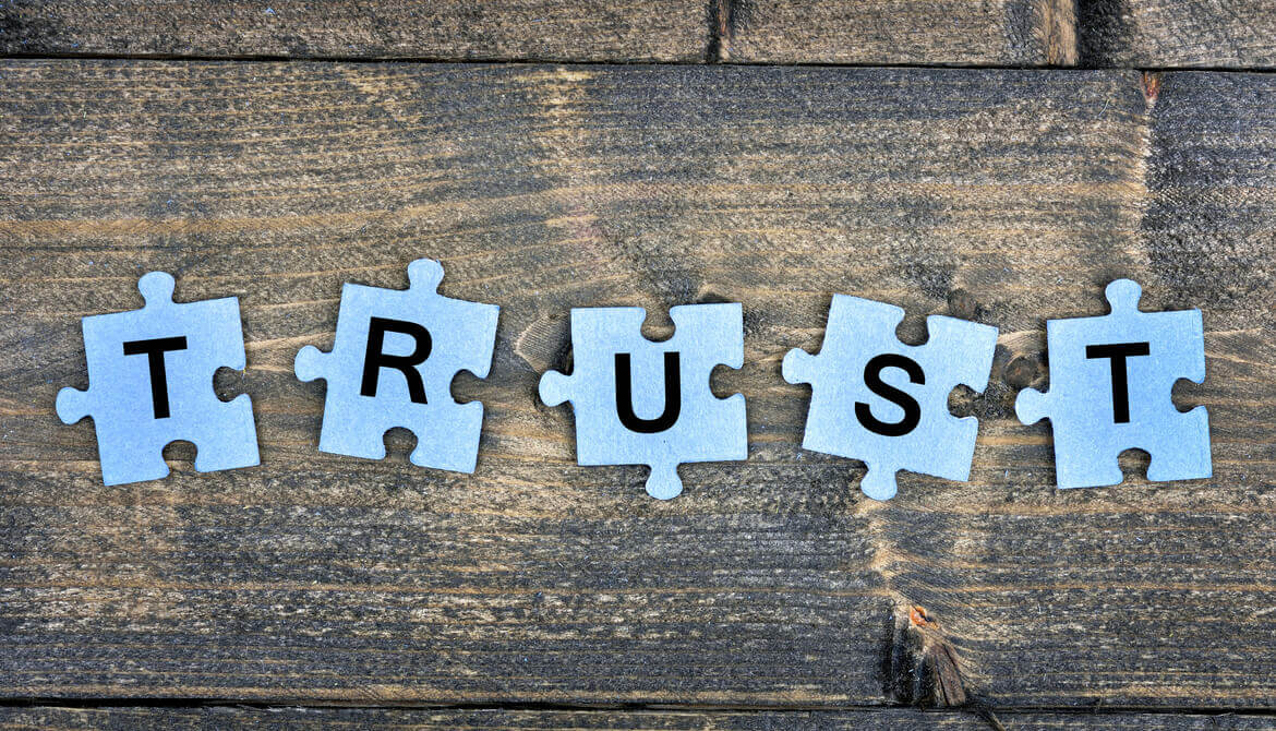 Letters of word TRUST spelled on blue puzzle pieces on wooden table