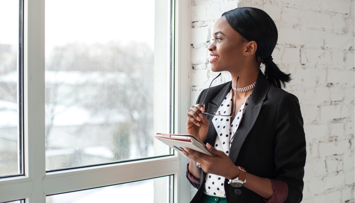 happy introverted businesswoman works alone on tablet while looking out window