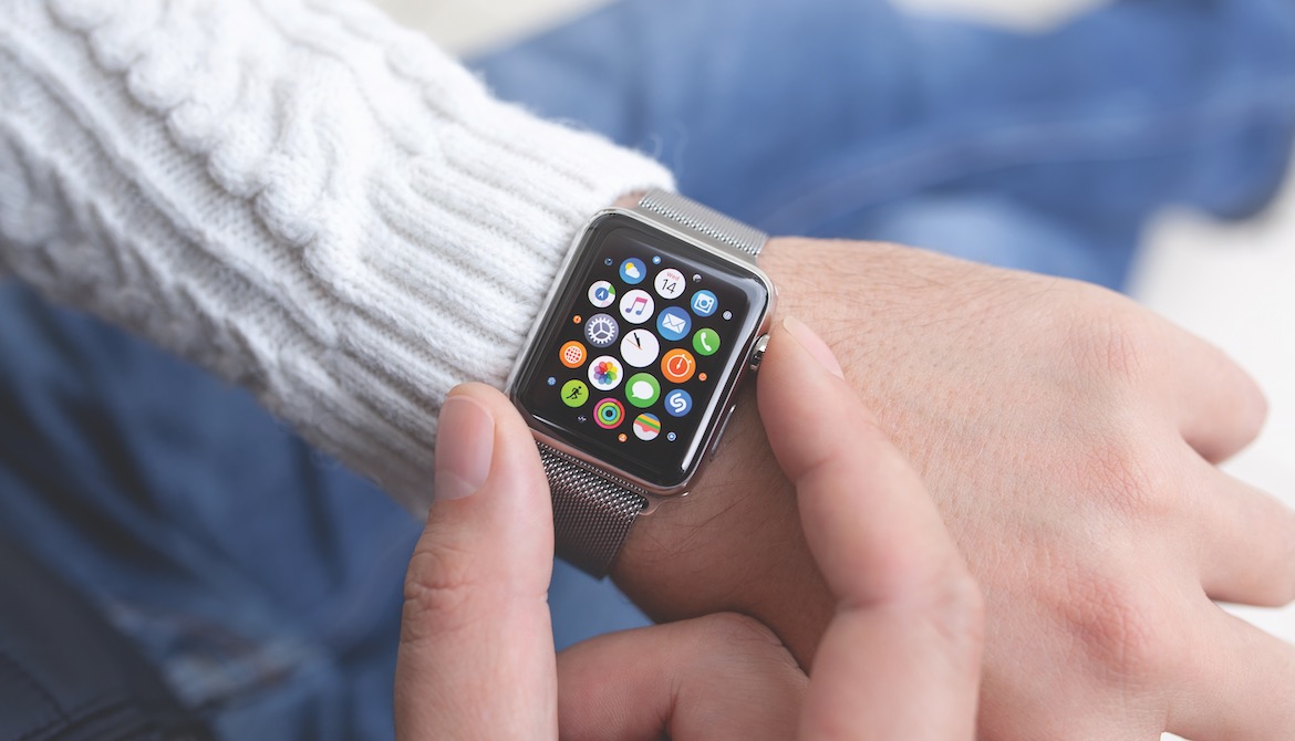 person in white sweater checking Apple Watch displaying colorful icons