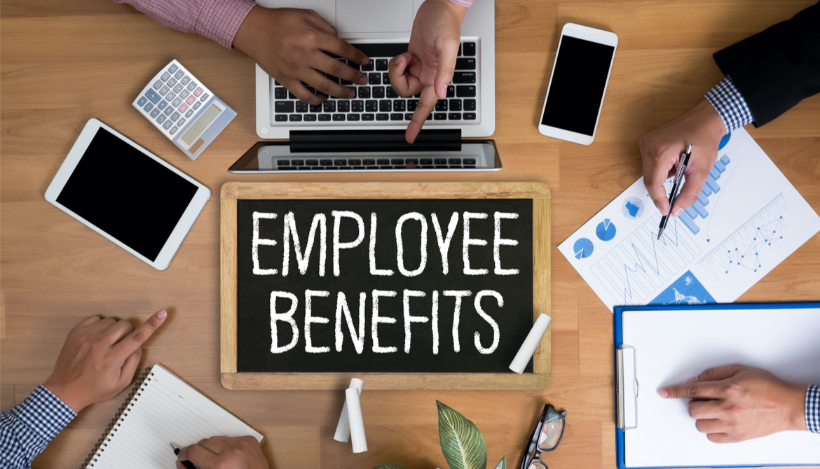 employee benefits written on small chalkboard on a table with three employees working at it