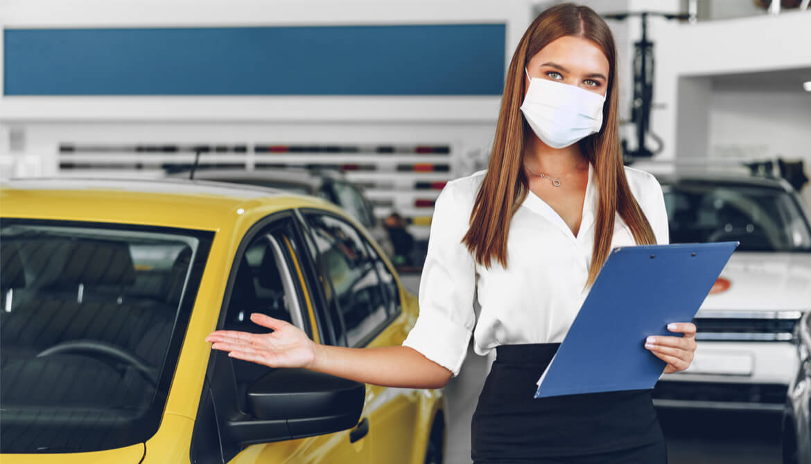 female car salesperson holding arm out by car