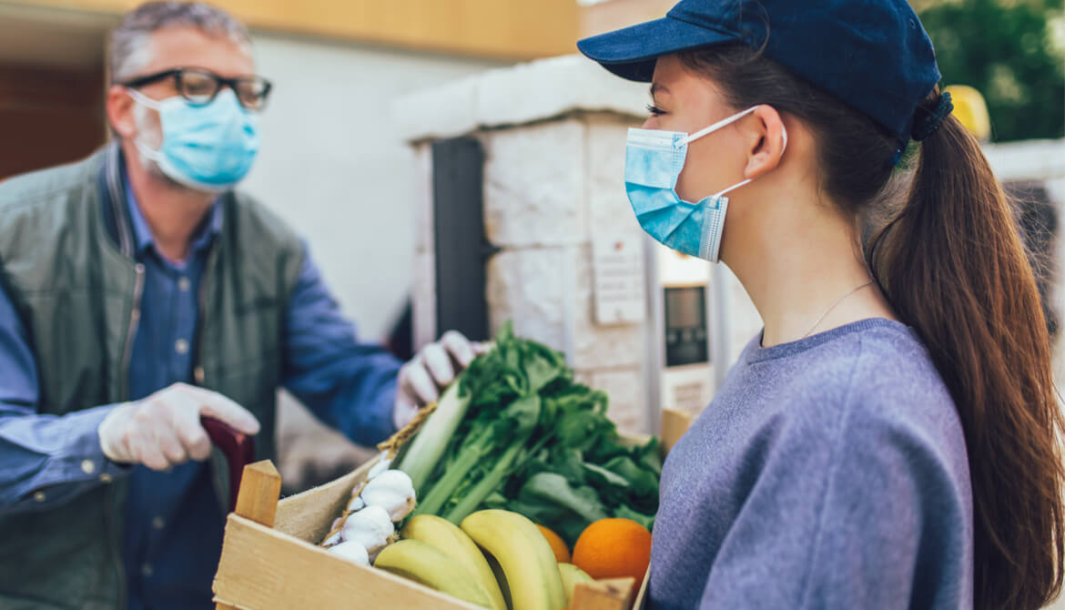 young woman in mask delivers box of groceries to elderly man during pandemic