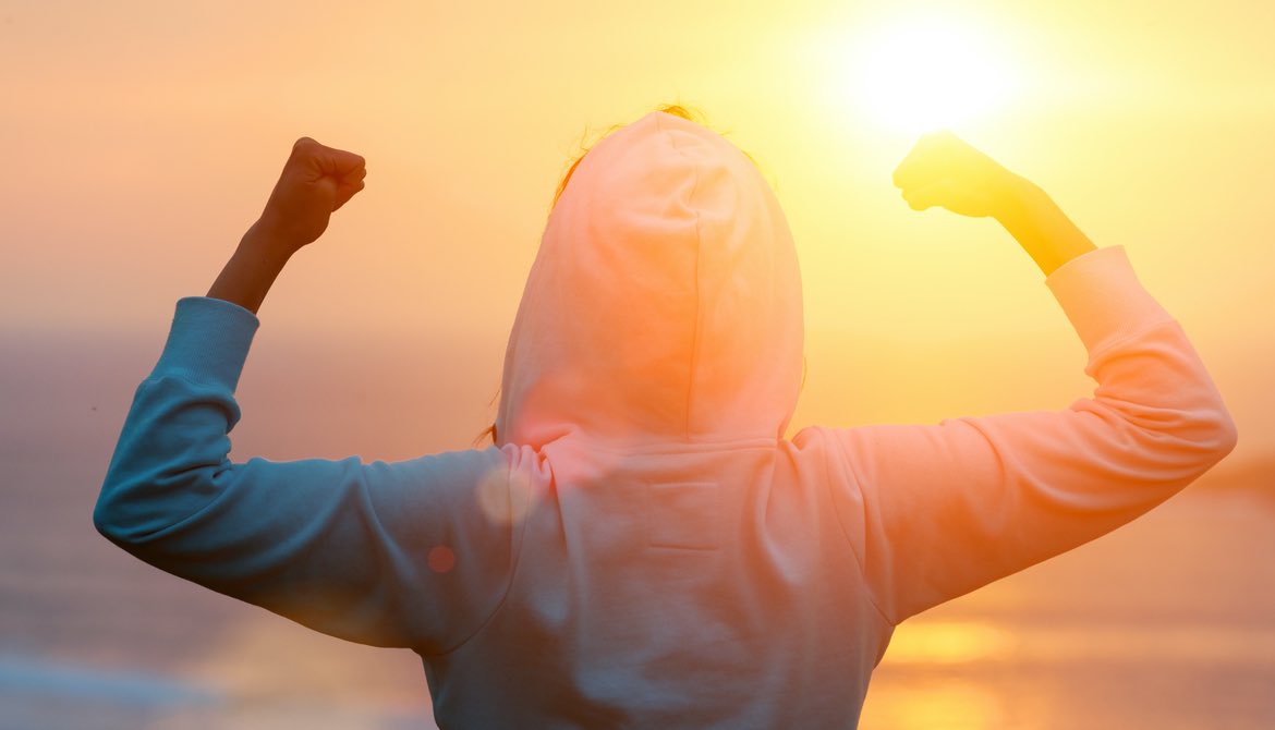 Back view of strong motivated woman celebrating goals towards the sun