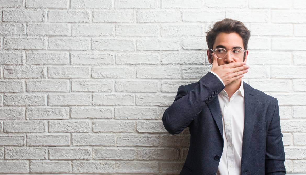 man covering mouth with hand standing by white wall