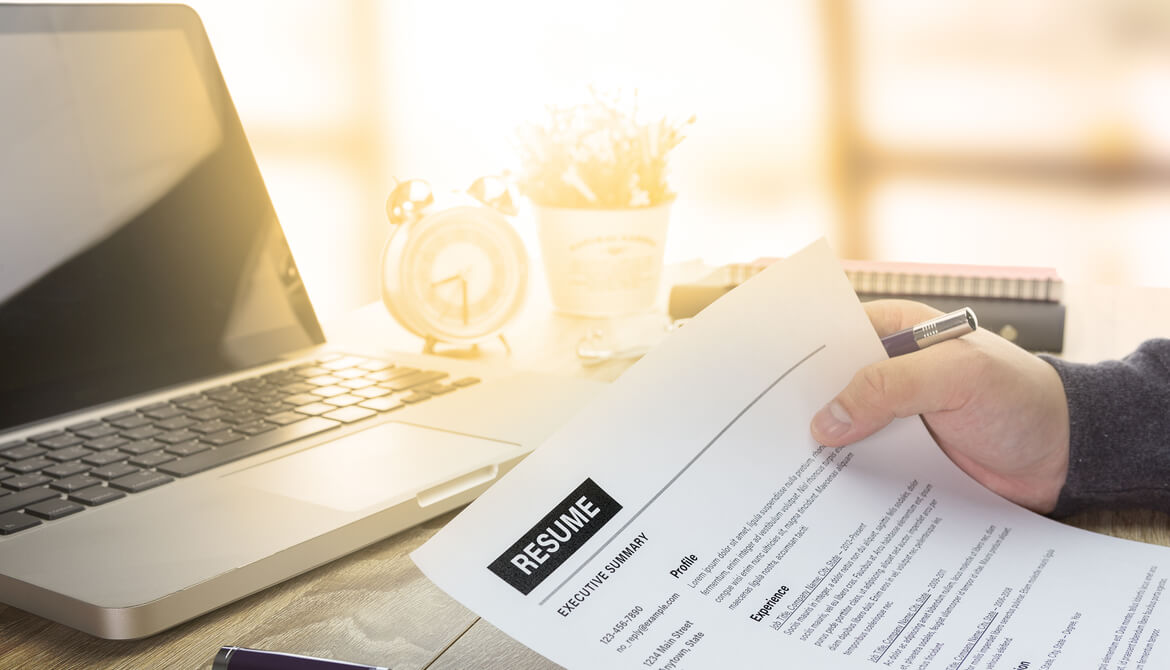 hand with pen holding a printed resume to review in sunny office