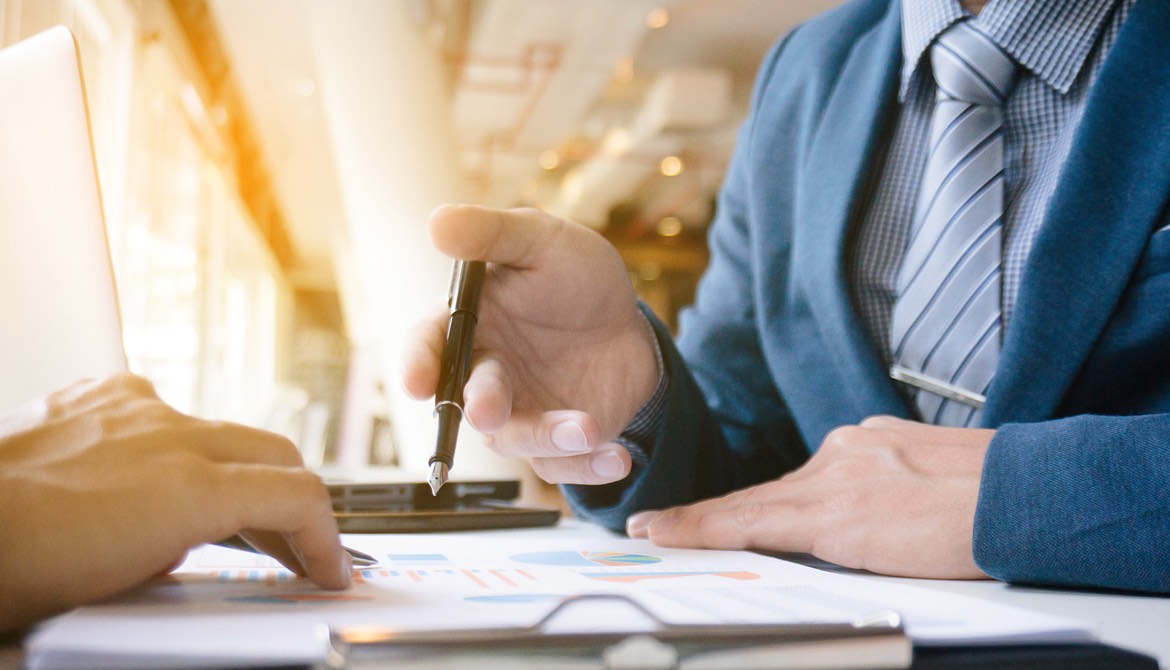 businessman in tie holding pen and gesturing to a report while colleague reviews