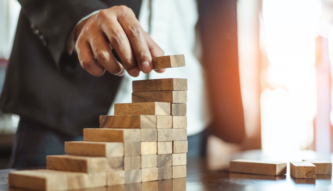 hand of businessman in suit building a growing staircase out of wooden blocks