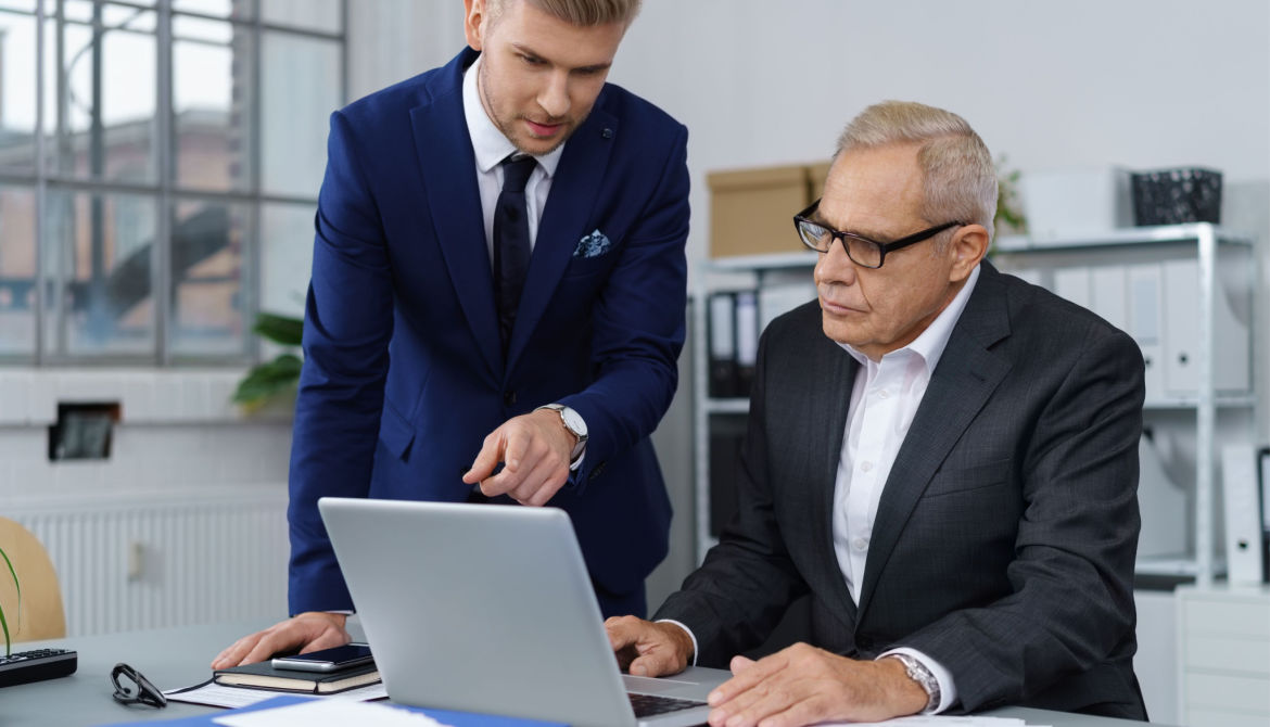 mature executive and young executive work on laptop in office