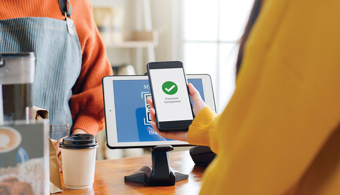 woman in yellow sweater uses mobile tap-to-pay at a café