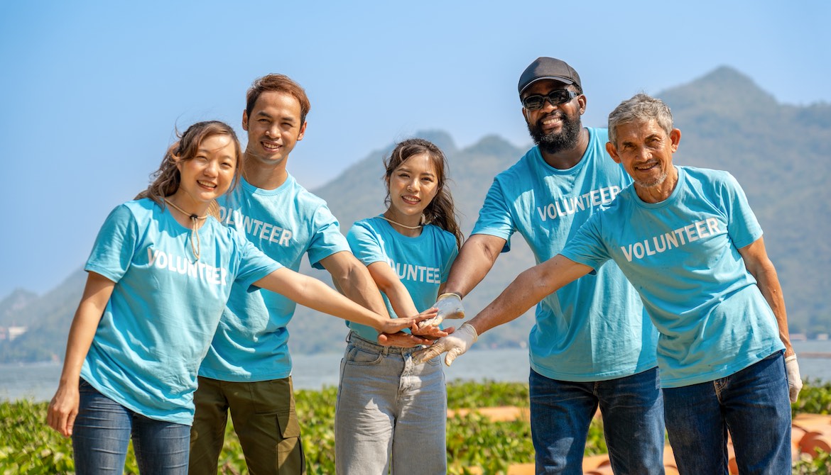 Diverse group of corporate volunteers stack hands together to kick off charitable volunteer project