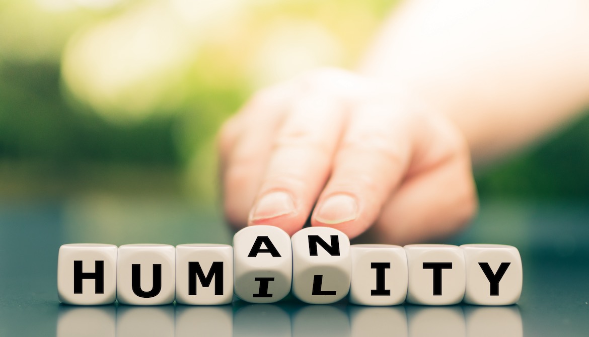 hand switching the middle letters of the word HUMANITY to HUMILITY