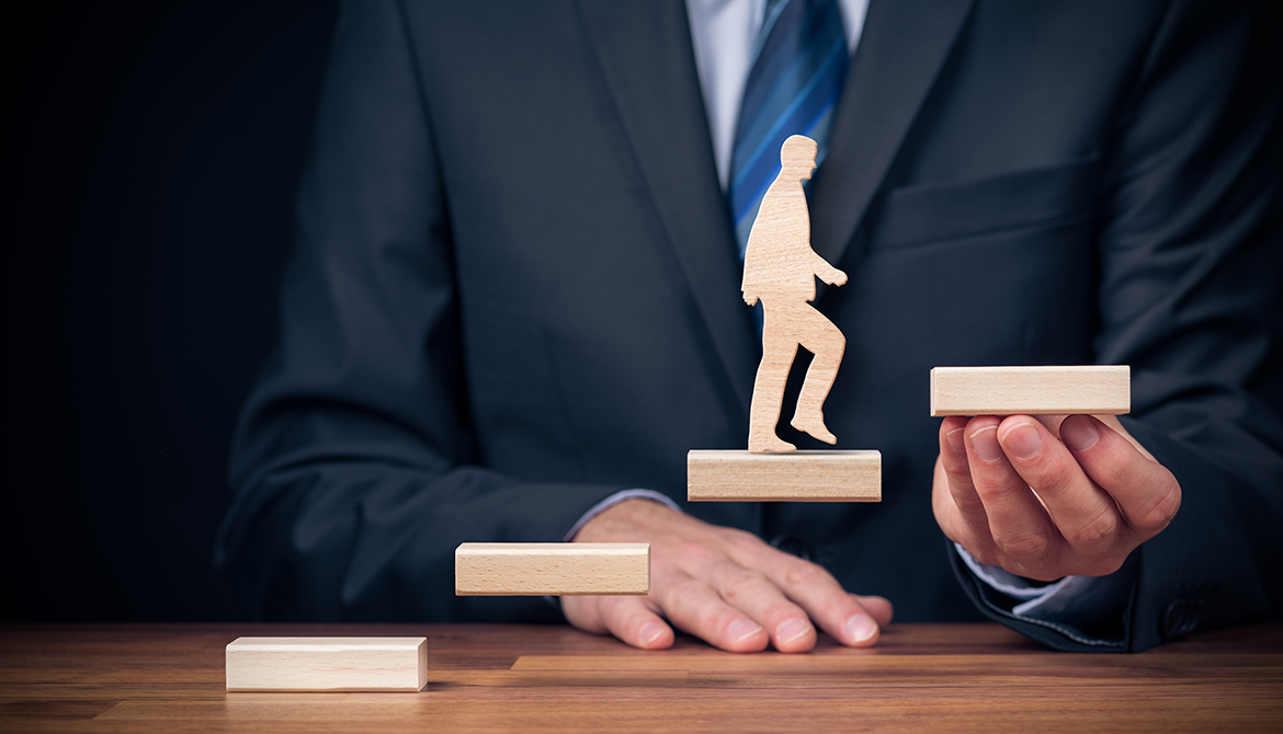 man holding wooden blocks creating stairs for wooden man to climb