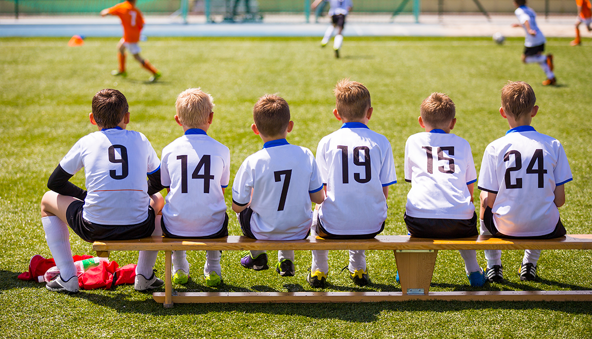 children's sports team sitting on the bench watching the game