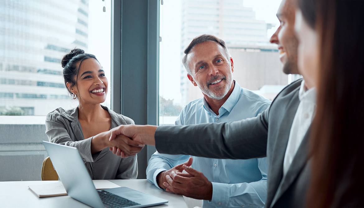 individuals shaking hands over laptop
