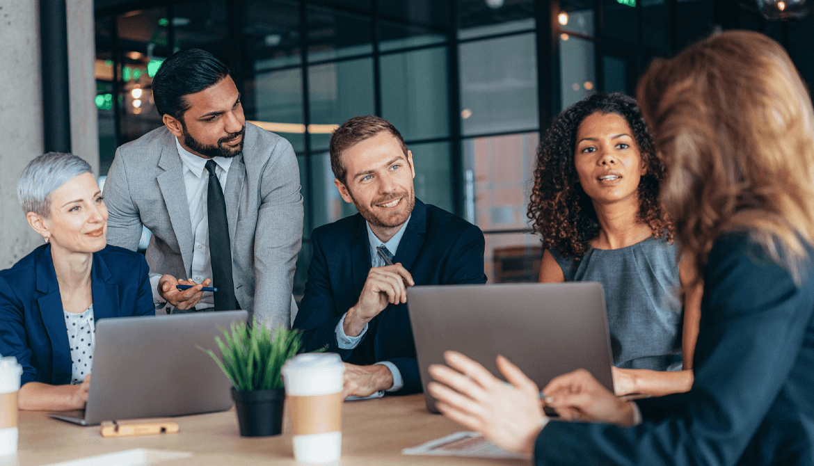 individuals sitting around a table looking over a laptop