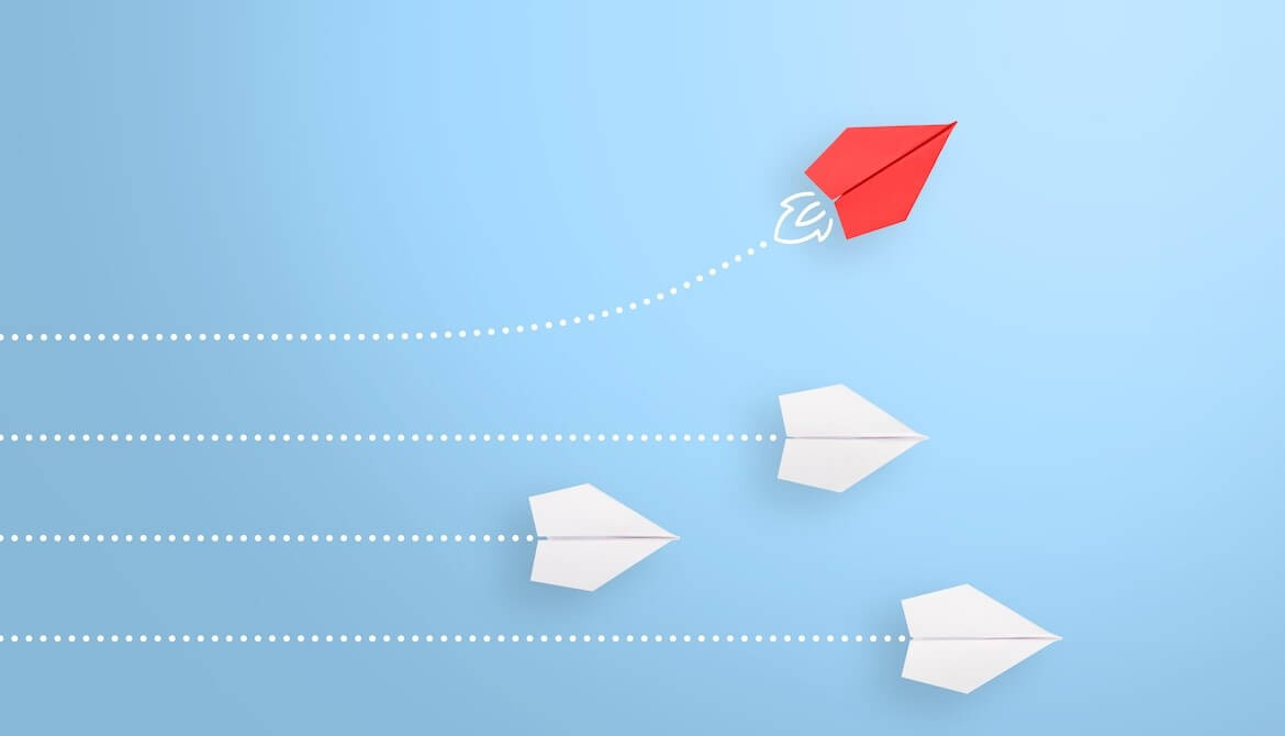 one red paper airplane flying it's own course away from 3 white paper airplanes