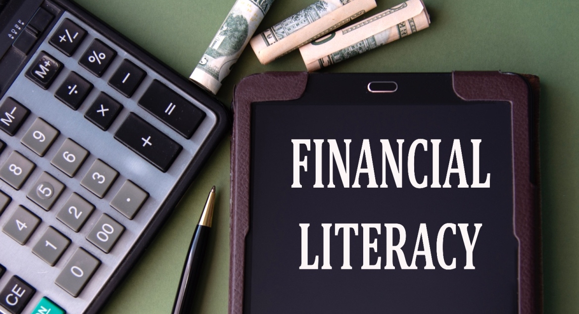 FINANCIAL LITERACY words appear on the screen of a tablet next to a calculator and banknotes