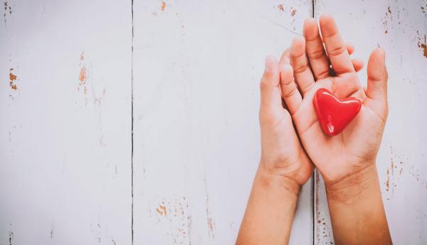 hands holding a red heart over a white wooden background