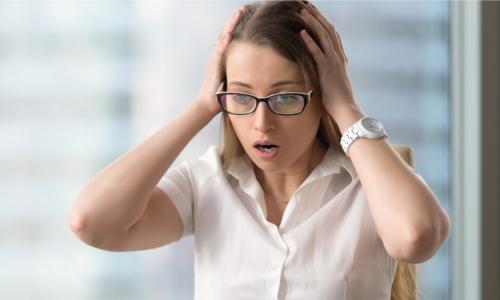 young businesswoman clutching her head and making a horrified face