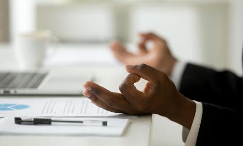 businessman meditates at his desk to practice better mental health in the workplace