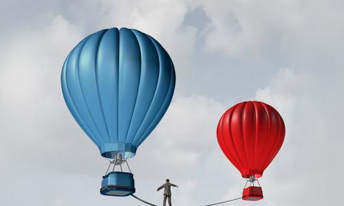 A business man walks a tight rope from a blue hot air balloon to a red one