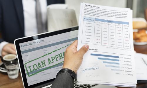 two businessmen working on a marketing plan over a laptop that displays Loan Approved