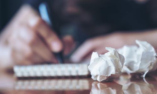 crumpled pieces of paper in front of a person writing pitches in a notebook