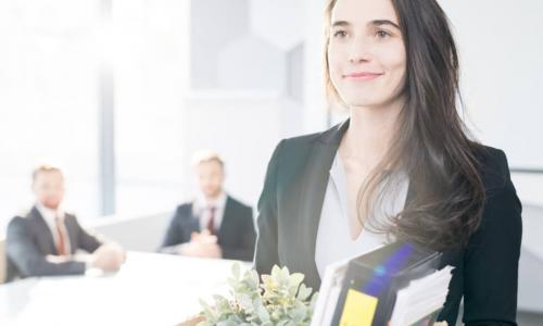 smiling young businesswoman holding box of personal belongings leaving office after quitting job