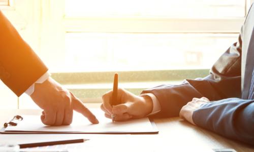 businessman pointing to a contract being signed by another man with a pen