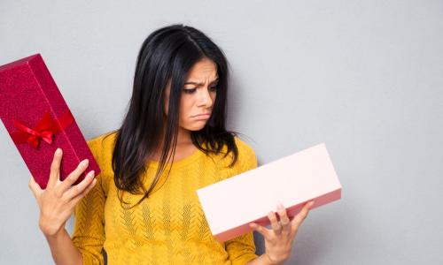 young woman in yellow sweater looking sadly into an open holiday gift box