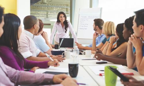 Team of employees around a table listening to meeting leader