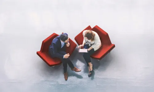 man and woman sitting in red chairs have a discussion