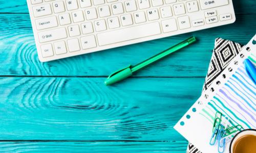 Pens and notebook next to a keyboard on a green wooden desktop