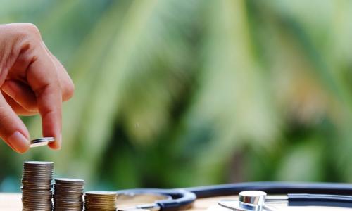 hand adding to stacks of coins next to a notebook and stethoscope representing financial wellness