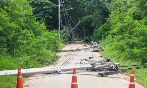 Downed power lines and telephone poles laying on a street in behind orange safety cones