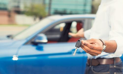 African American man holding out keys to a new blue car